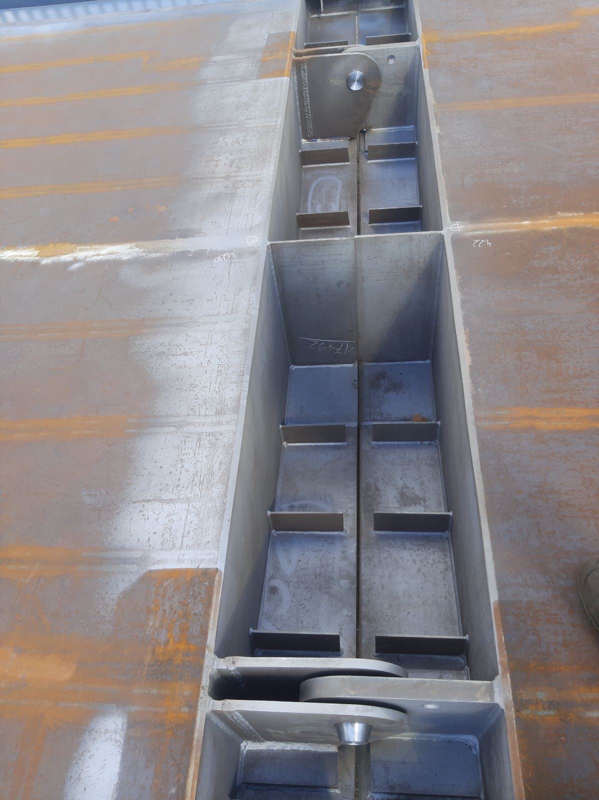 Metalowa konstrukcja hali w trakcie budowy, widoczne spawy i elementy mocujące, surowy metal z rdzawymi zaciekami.