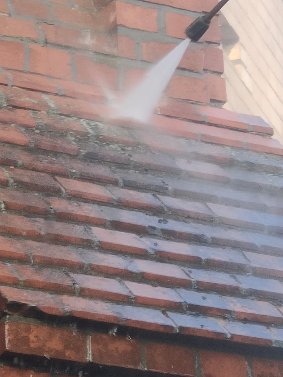 Czerwona dachówka czyszczona strumieniem wody pod ciśnieniem, widoczny fragment muru z cegły i dysza lancy myjącej