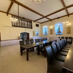 Ustawione stoły i krzesła w przestronnej sali bankietowej z drewnianymi belkami stropowymi i kryształowymi żyrandolami przed przygotowaniem do uroczystości.