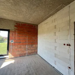 Wnętrze w stanie surowym w Trzebnicy z widoczną instalacją elektryczną w ścianach z pustaków i cegły, okablowanie prowadzone natynkowo.