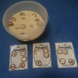 Miska z ryżem i ukrytymi obrazkami oraz trzy karty z narysowanymi słoikami z miejscami na obrazki, leżące na niebieskiej macie edukacyjnej.