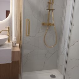 T home Tomasz Bokuniewicz - Nowoczesna łazienka z kabiną prysznicową typu walk-in, armatura w kolorze złota, umywalka nablatowa i marmurowe płytki na ścianach.