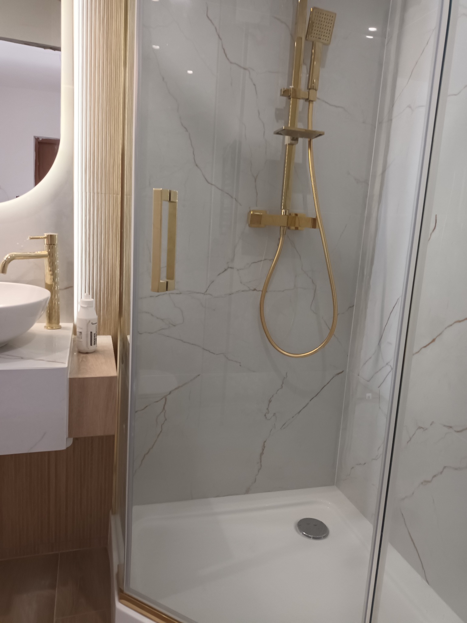 Nowoczesna łazienka z kabiną prysznicową typu walk-in, armatura w kolorze złota, umywalka nablatowa i marmurowe płytki na ścianach.