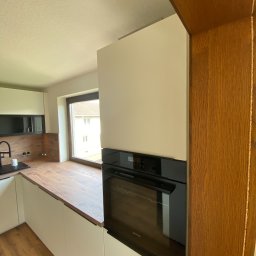 Gregor Möbel - Nowoczesna kuchnia z białymi frontami, drewnianym blatem i zabudowanym piekarnikiem Siemens, widok z perspektywy wnętrza, z oknem w tle.