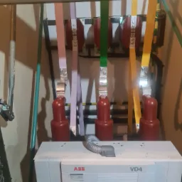 Rozdzielnica elektryczna ABB VD4 z kolorowymi przewodami fazowymi (różowy, zielony, żółty) i szarą rurką karbowaną, widoczne połączenia śrubowe i oznaczenia na urządzeniu.