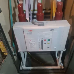 Rozdzielnica elektryczna ABB VD4 z trzema przewodami zasilającymi oznaczonymi kolorami: żółtym, fioletowym i zielonym, umieszczona w szarej obudowie z metalową siatką po lewej stronie.