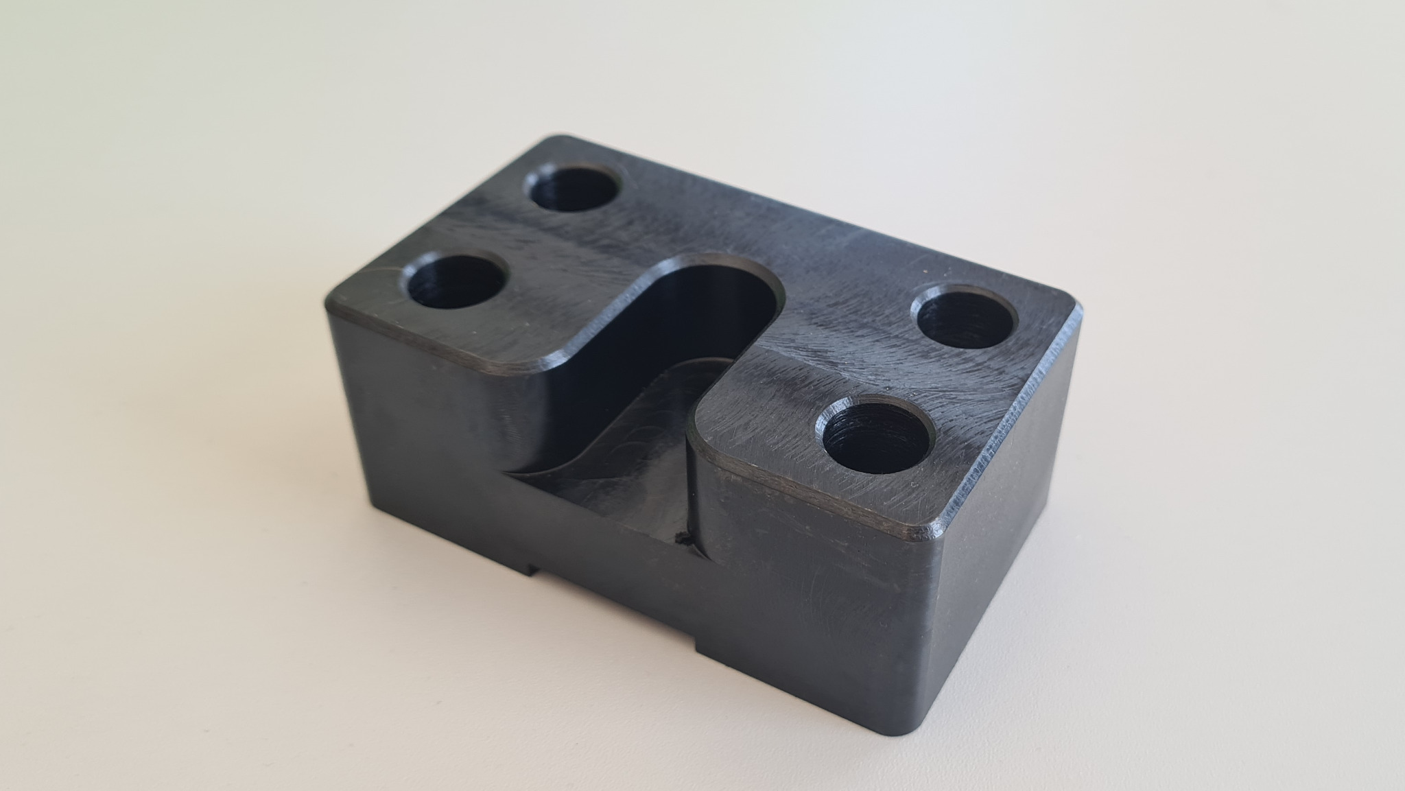 Czarny, precyzyjnie wykonany element z tworzywa sztucznego z widocznymi otworami i wycięciem w kształcie litery 'S', leżący na jasnym tle.