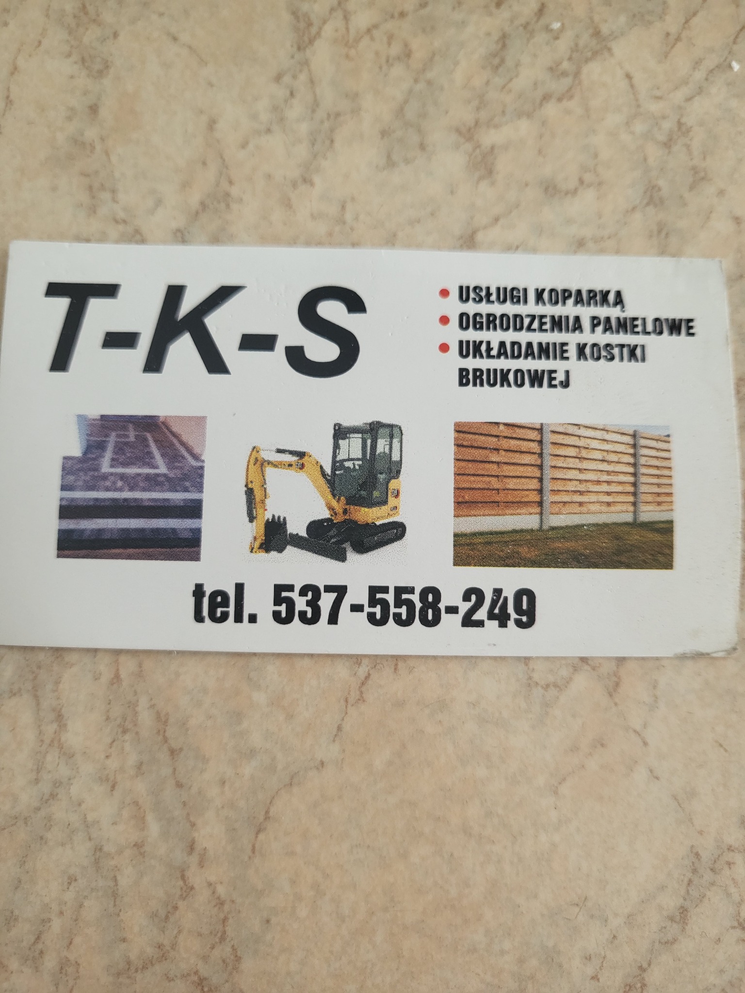 Wizytówka firmy T-K-S oferującej usługi koparką, ogrodzenia panelowe oraz prace brukarskie, z miniaturami zdjęć kostki brukowej, koparki i ogrodzenia oraz numerem telefonu.