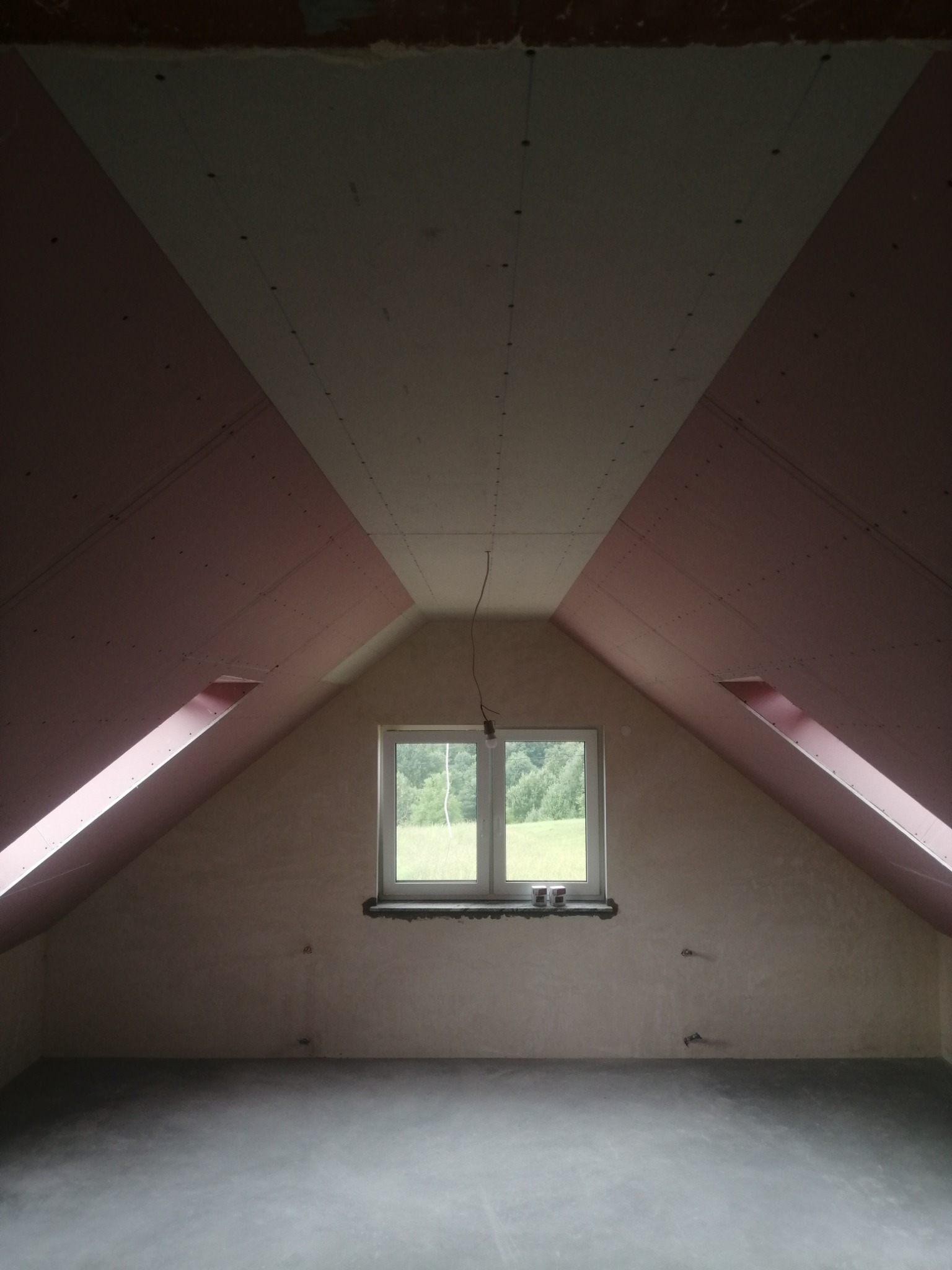 Poddasze po montażu płyt karton-gips, widoczne łączenia płyt na suficie i skosach, okno z widokiem na zieleń.