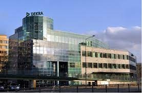 Nowoczesny budynek biurowy z przeszkloną fasadą i logo DEKRA na dachu, widoczny na tle błękitnego nieba z chmurami.
