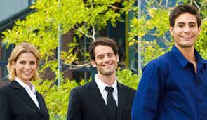 Uśmiechnięci pracownicy: kobieta w czarnym garniturze, mężczyzna w garniturze z krawatem oraz mężczyzna w niebieskiej koszuli na tle zieleni.