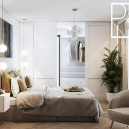 Jasna sypialnia z łóżkiem, szafą wnękową za przesuwnymi drzwiami, lampami wiszącymi i fotelem, na podłodze parkiet ułożony w jodełkę.