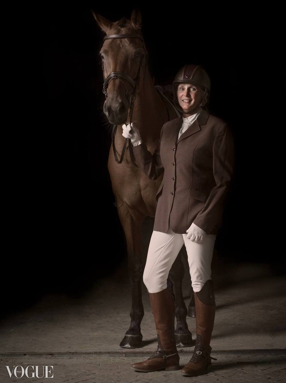 Portret kobiety w stroju jeździeckim, stojącej obok konia na ciemnym tle, stylizowane zdjęcie modowe.