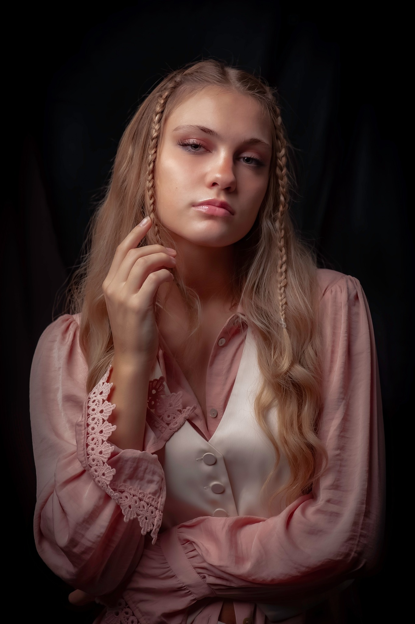 Portret młodej kobiety z blond włosami upiętymi w warkocze, ubrana w różową bluzkę z koronkowymi wykończeniami i białą kamizelkę na ciemnym tle.