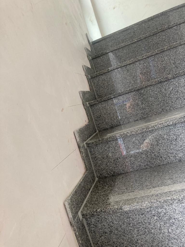 Granitowe schody wewnętrzne z szarego kamienia z widocznymi fugami, przylegające do pomalowanej ściany w jasnym odcieniu.