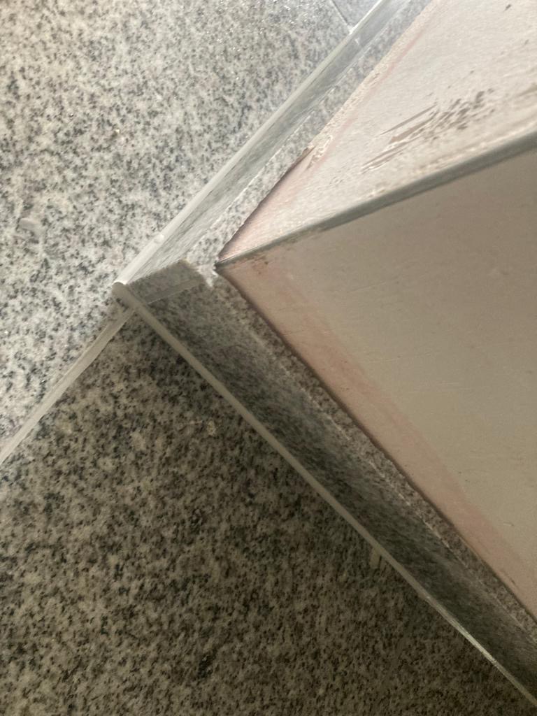 Szczegółowe ujęcie narożnika ściany wykończonego szarą, nakrapianą płytką ceramiczną, z widoczną fugą i nierównościami na krawędzi płytki przylegającej do ściany.