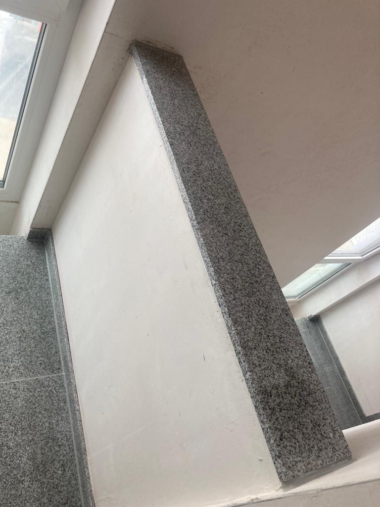 Wykończenie schodów wewnętrznych szarym granitem, widoczne fragmenty okna i sufitu.