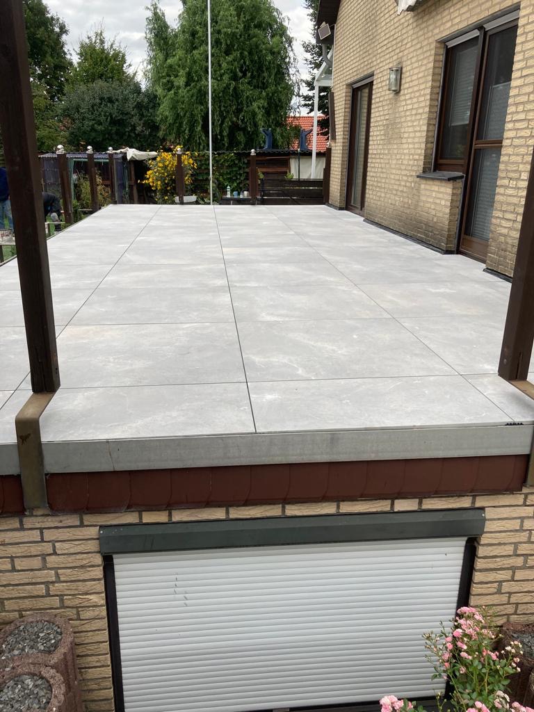 Wyłożony jasnoszarą płytką taras w Lublińcu, widok z dołu, z widocznymi elementami konstrukcyjnymi tarasu i fragmentem elewacji budynku.