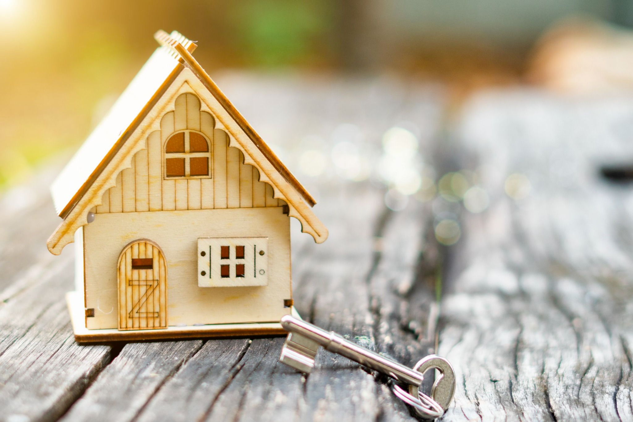 Drewniany model domu z kluczem na tle postarzanego drewna, delikatne, rozproszone światło słoneczne.