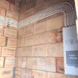 Białe rurki peszel ułożone równolegle na surowej ścianie z cegły dziurawki, z zamontowaną puszką podtynkową z boku.