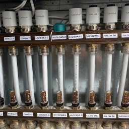 Usługi budowlane Majerczyk - Rozdzielacz ogrzewania podłogowego z termostatami Salus, oznaczony dla różnych pomieszczeń: pokój L, P, T, łazienka G, kotłownia, łazienka D, salon WYJ., salon ŚR., salon STÓŁ, kuchnia, wiatrołap.