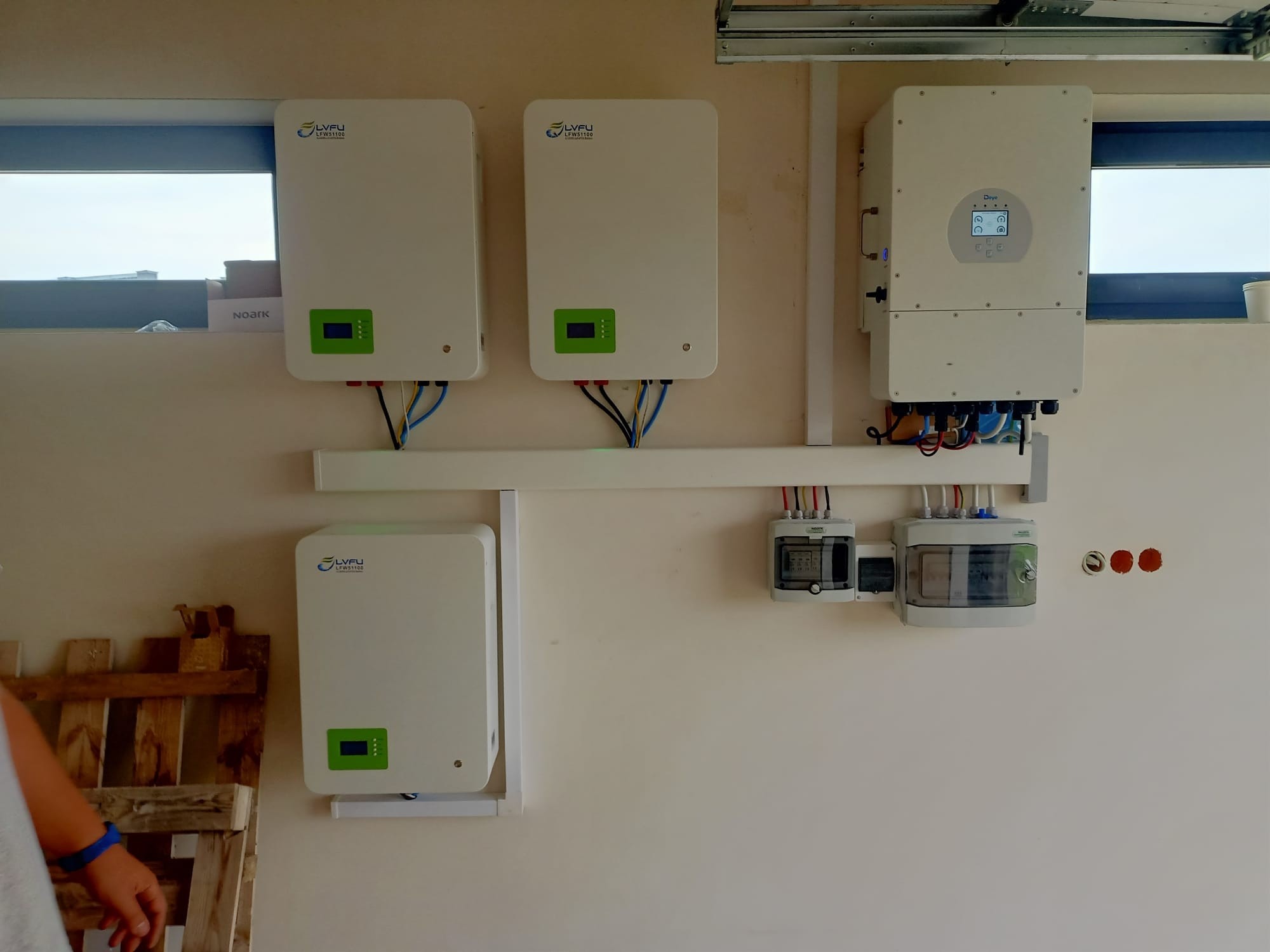 Instalacja wewnętrzna: trzy białe moduły magazynu energii LVFU LFW51100 z zielonymi wyświetlaczami, falownik Deye z ekranem LCD, zabezpieczenia i okablowanie na ścianie w garażu.