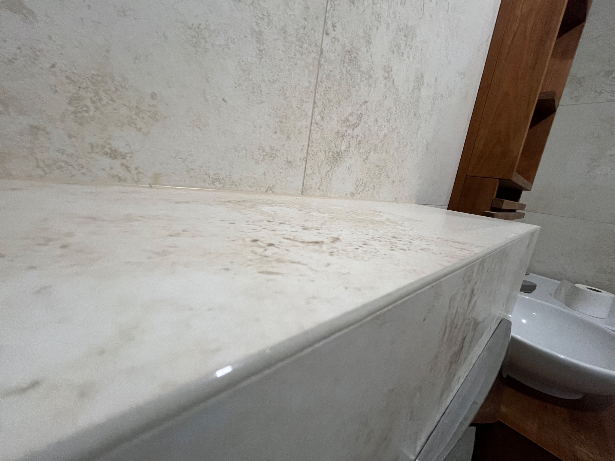 Blat umywalki z beżowego marmuru z widoczną strukturą, zamontowany w łazience, obok drewniany regał i biała umywalka.