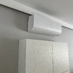 Biała klimatyzacja Haier na szarej ścianie nad szafką z heksagonalnym wzorem. Nowoczesny design, minimalistyczne wnętrze, delikatne oświetlenie.