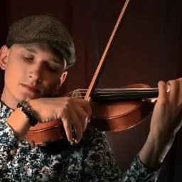 Młody mężczyzna w kaszkiecie, z zamkniętymi oczami, gra na skrzypcach, ubrany w koszulę w kwiaty, na ciemnym tle.