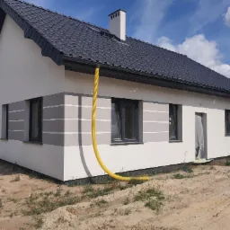 Nowoczesny dom jednorodzinny w Wałbrzychu z jasną elewacją w odcieniach szarości, ciemną dachówką i widoczną żółtą rurą wentylacyjną przy elewacji.