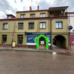 Fasada budynku z szyldem 'CUK Ubezpieczenia' ozdobiona zielonym łukiem z balonów nad wejściem.