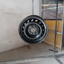 Błyszcząca, czarna felga stalowa zawieszona na przewodzie w warsztacie, po procesie malowania.