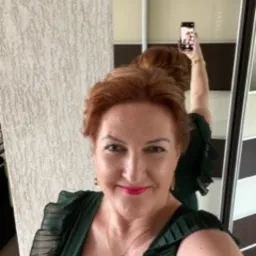 Kobieta z rudymi włosami w zielonej sukience robi selfie w lustrze, widoczny fragment wnętrza biura.