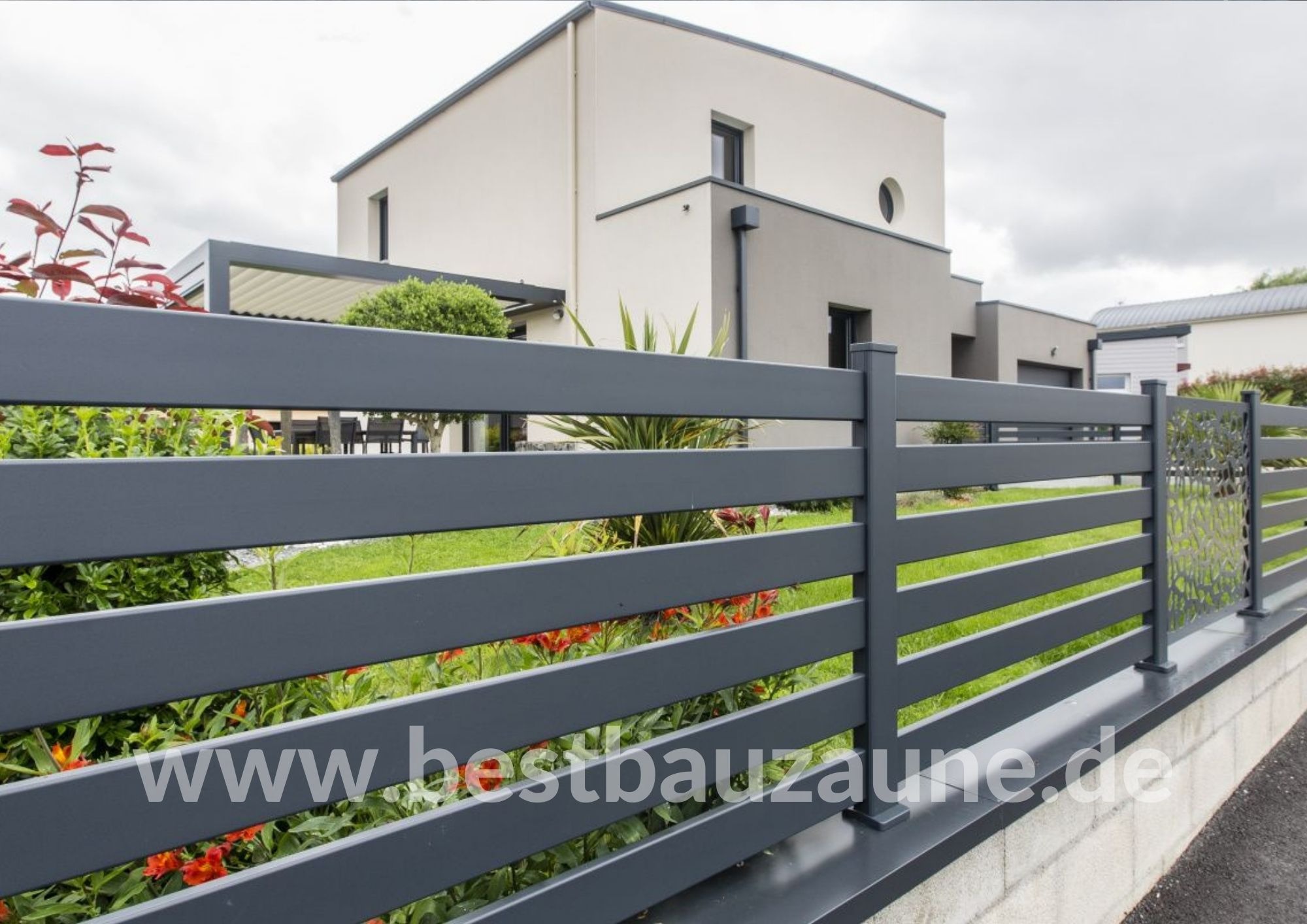 Nowoczesne ogrodzenie panelowe w kolorze grafitowym z poziomymi szczeblami i dekoracyjnym ażurowym panelem, na tle nowoczesnego domu z ogrodem.
