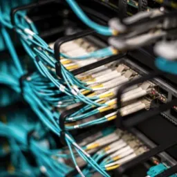 Zorganizowane okablowanie światłowodowe w serwerowni w Warszawie, z przewagą niebieskich kabli, prowadzone w metalowych korytkach. Widoczne panele krosownicze i urządzenia sieciowe w tle.