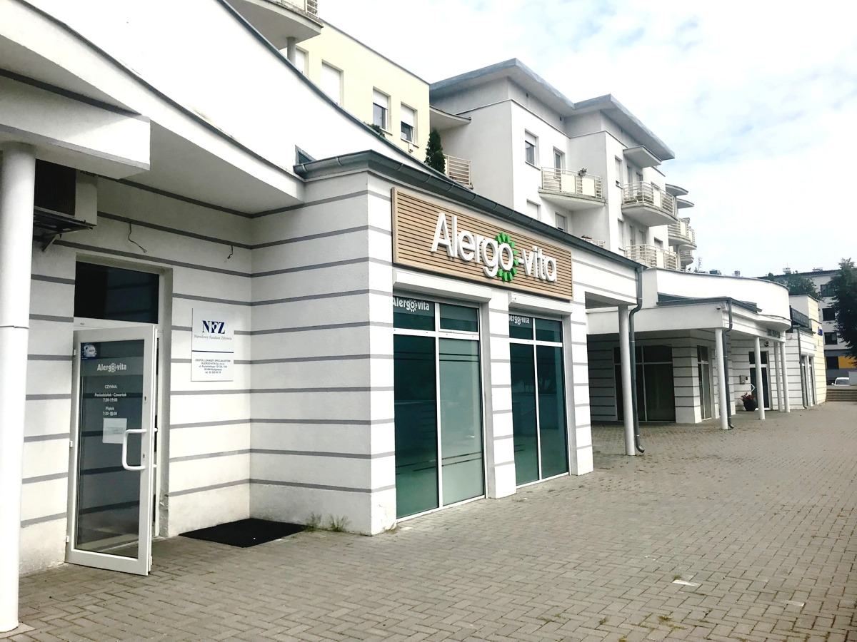 Fasada budynku z szyldem Alergo-vita, widok z zewnątrz na wejście i okna lokalu.