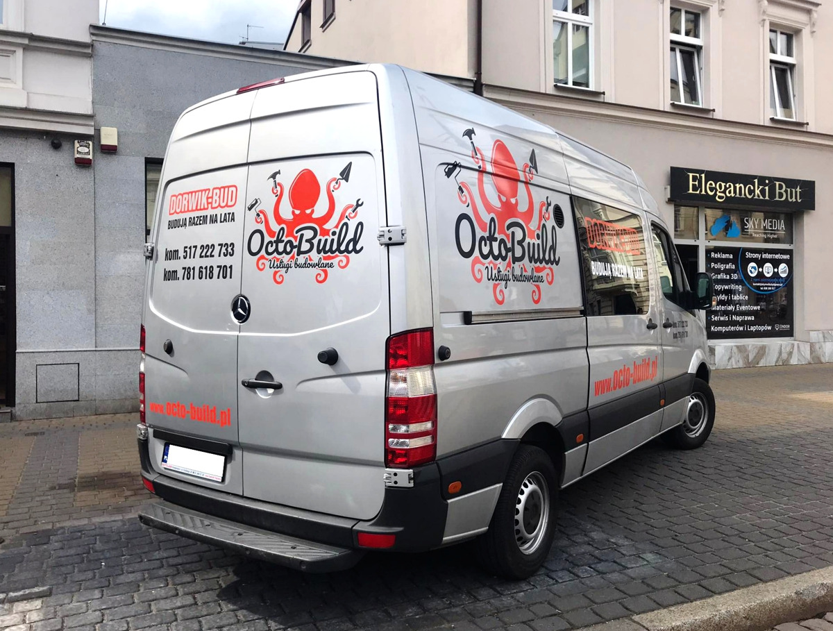 Srebrny van Mercedes z logo firmy budowlanej OctoBuild z ośmiornicą trzymającą narzędzia, zaparkowany na ulicy z kostki brukowej przed budynkiem z szyldem Eleganciki But i Sky Media.