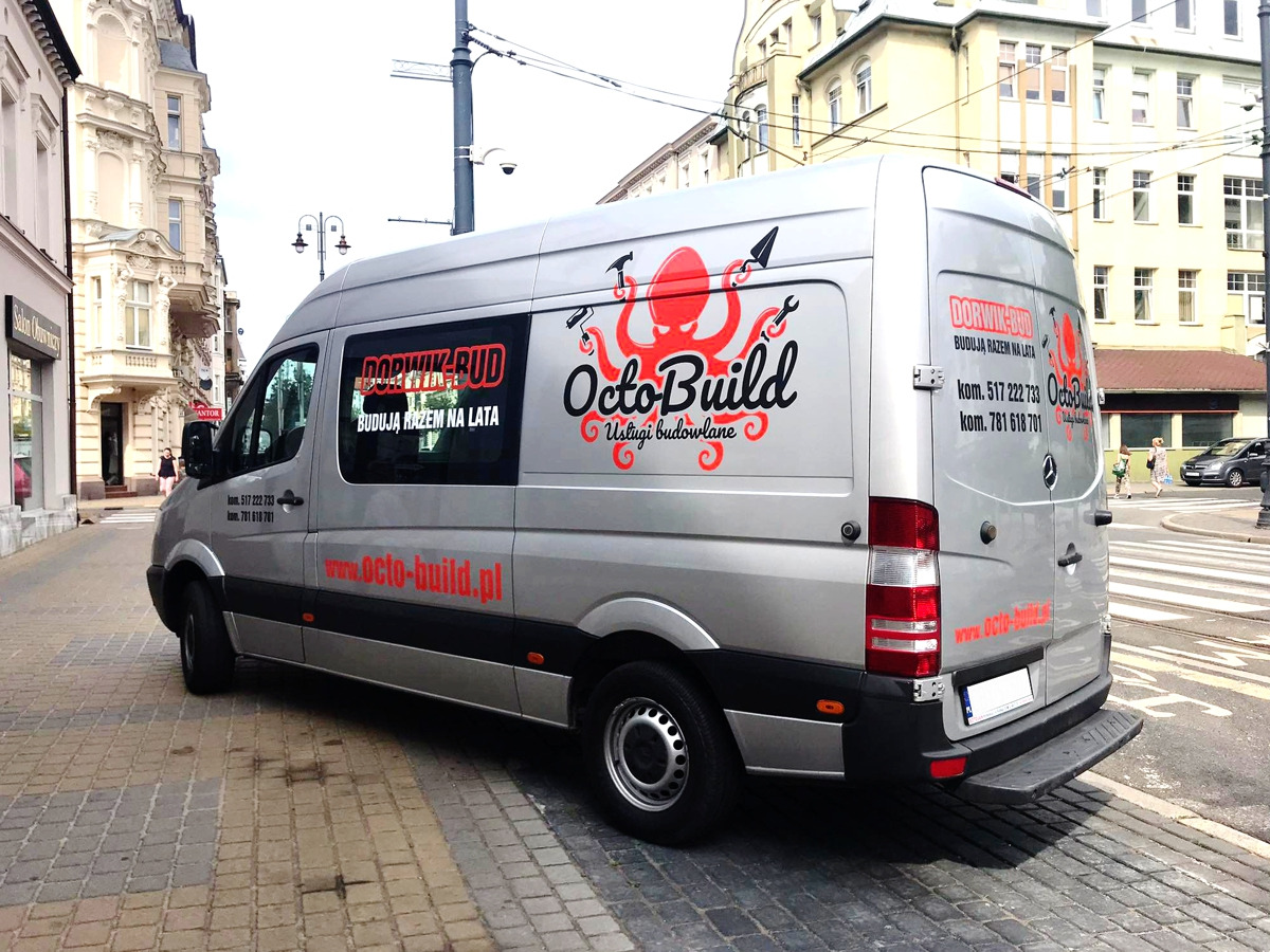Srebrny samochód dostawczy firmy budowlanej z Bydgoszczy, z dużym logo ośmiornicy z narzędziami i napisem OctoBuild. Widoczne dane kontaktowe i adres strony internetowej. Tło stanowi fragment ulicy...