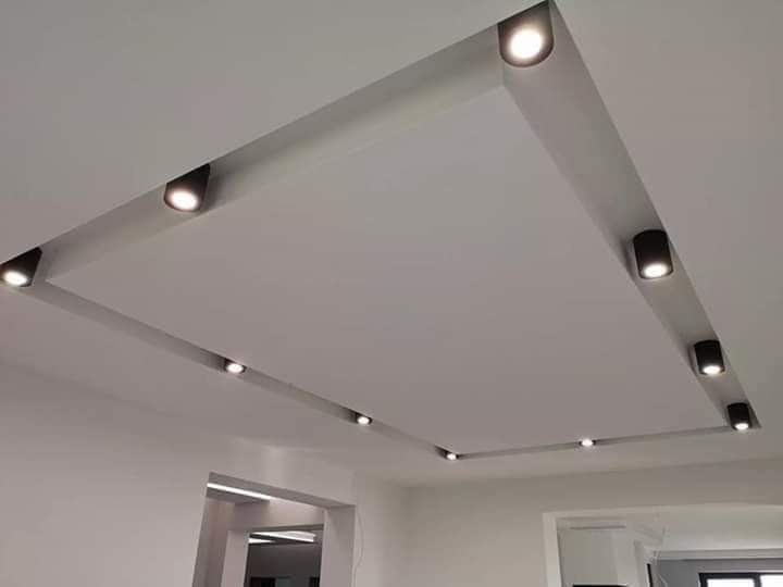 Nowoczesny sufit podwieszany z wbudowanymi, czarnymi reflektorami punktowymi, tworzącymi geometryczny wzór oświetleniowy w jasnym wnętrzu.