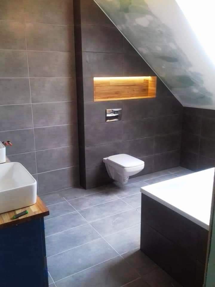 Nowoczesna łazienka w odcieniach szarości z podwieszaną miską WC, drewnianą wnęką z oświetleniem i umywalką na drewnianym blacie.