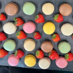 Aranżacja kolorowych makaronik&oacute;w i świeżych truskawek na ciemnoszarym, kamiennym tle, tworząca apetyczną kompozycję.