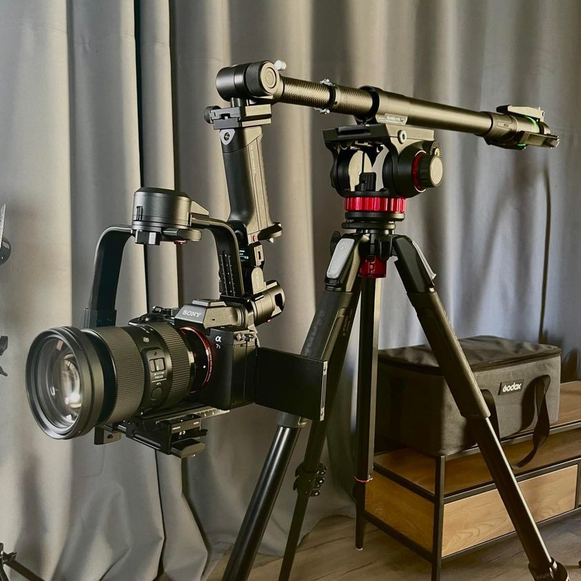 Profesjonalny zestaw do filmowania: kamera Sony Alpha z obiektywem na stabilizatorze i statywie z głowicą olejową, tło z szarych zasłon, torba Godox w tle.