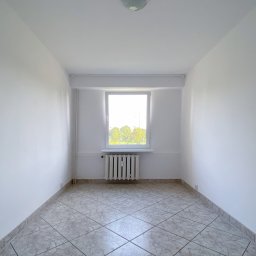 remonty wysoki standard - Puste, wyremontowane pomieszczenie z białymi ścianami, grzejnikiem pod oknem i podłogą wyłożoną płytkami w odcieniach szarości i beżu.