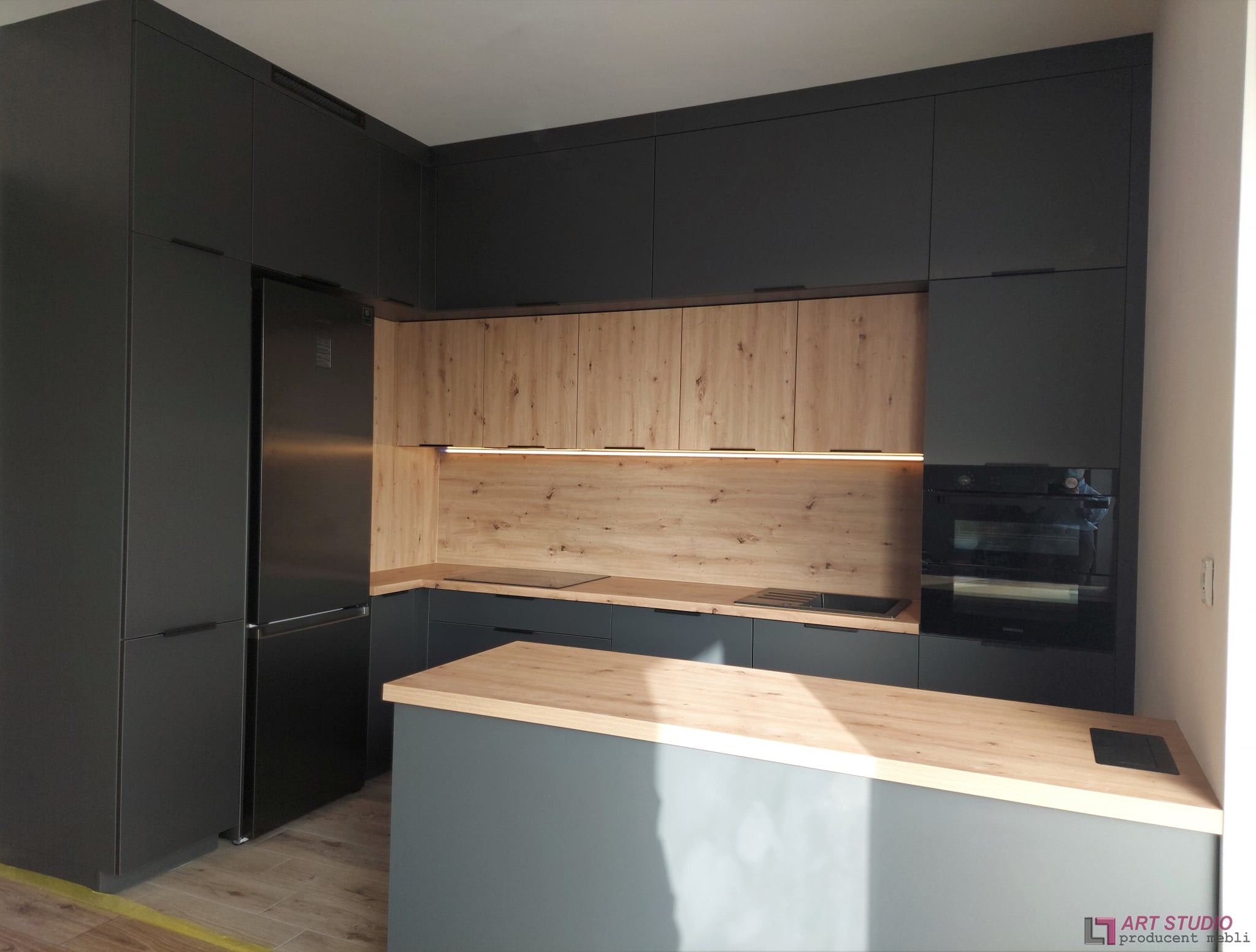 Nowoczesna kuchnia w odcieniach szarości i drewna z wyspą, oświetleniem LED podszafkowym i zabudowanym sprzętem AGD.