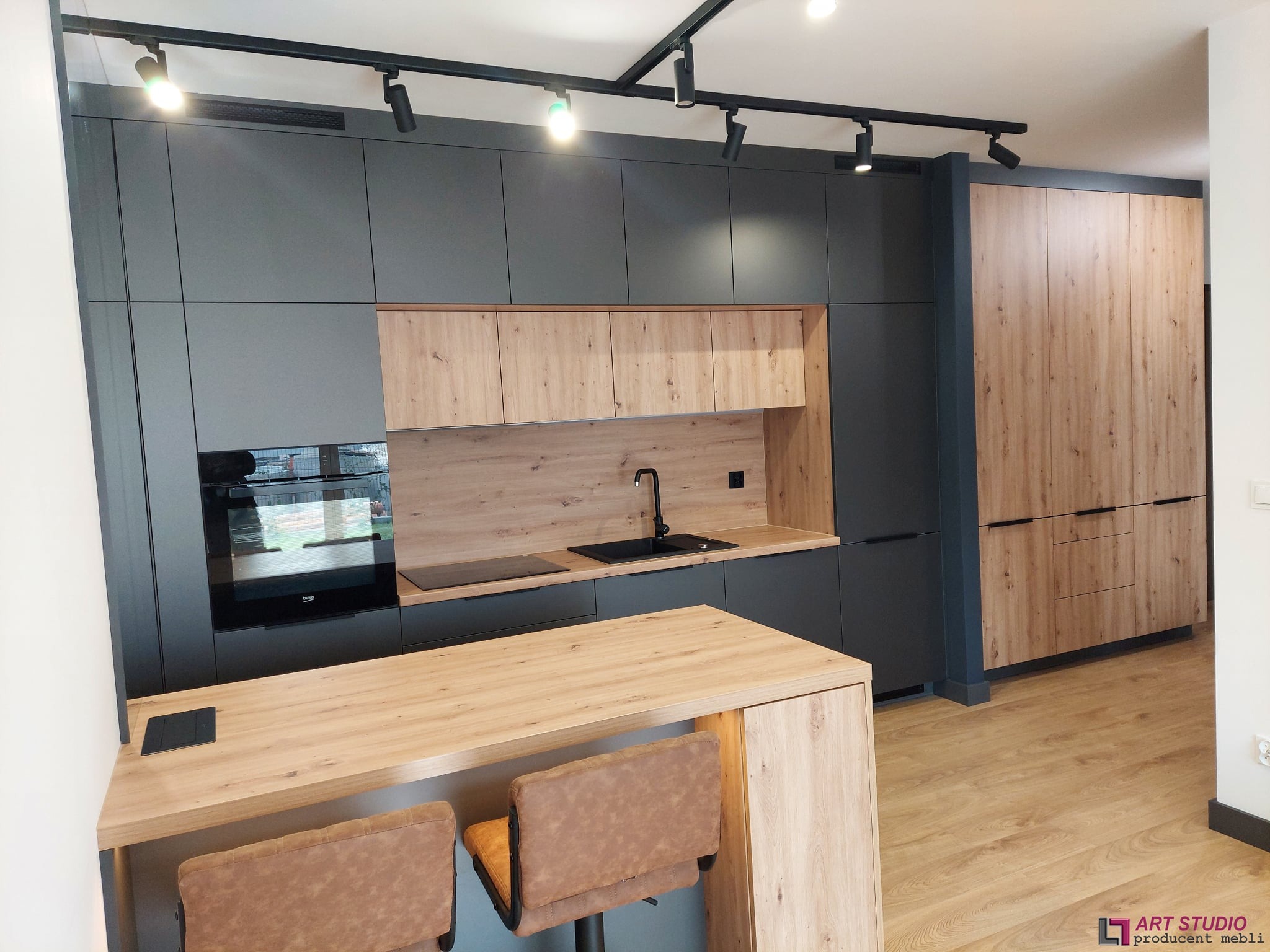 Nowoczesna kuchnia z szarymi szafkami i drewnianymi akcentami, wyspa z dwoma hokerami, oświetlenie punktowe na suficie.