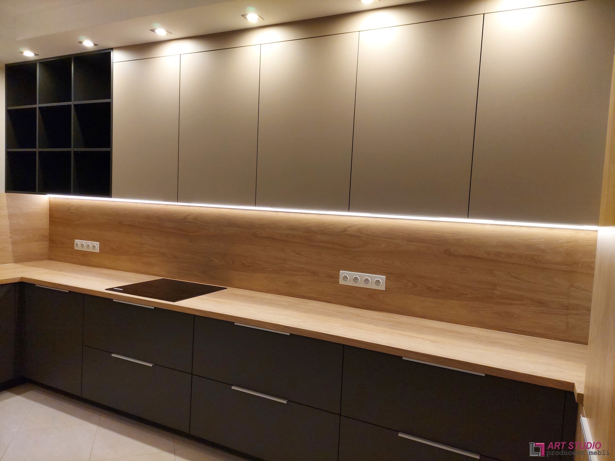 Nowoczesna kuchnia z beżowymi szafkami górnymi i ciemnoszarymi dolnymi, drewniany blat, oświetlenie LED pod szafkami, minimalistyczny styl.