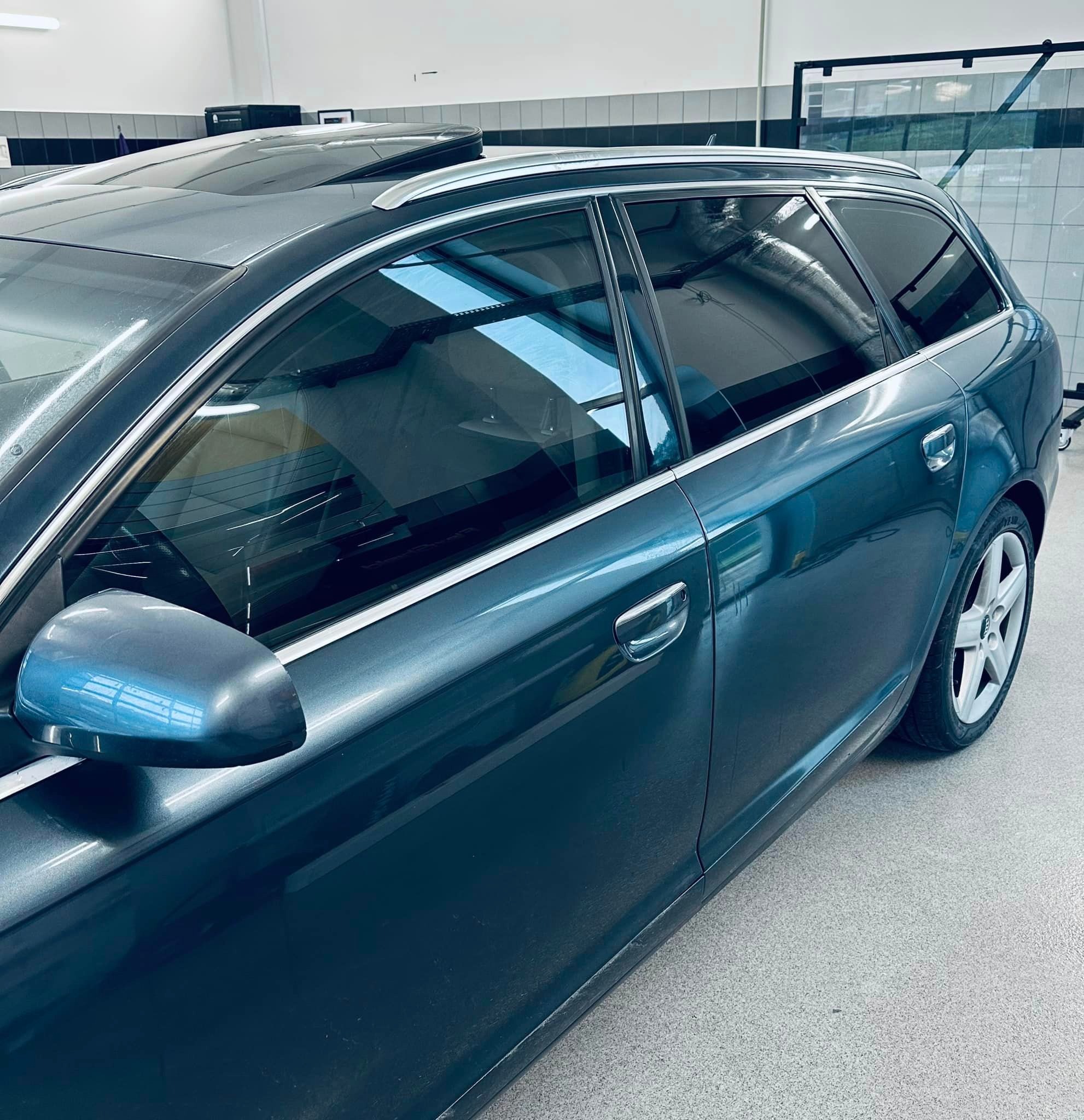 Granatowy samochód kombi z przyciemnionymi szybami w warsztacie, widoczne odbicia w szybach i karoserii.