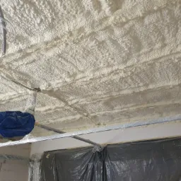 Piana izolacyjna PUR na suficie z widocznymi przewodami elektrycznymi, zabezpieczonymi elementami i folią ochronną na ścianie.