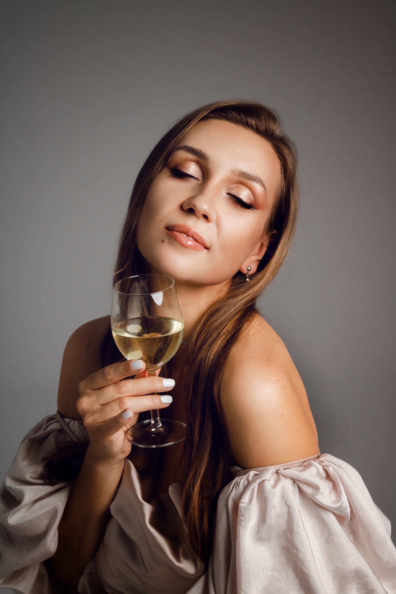 Kobieta z zamkniętymi oczami, z delikatnym makijażem w odcieniach złota, trzyma kieliszek białego wina w Łodzi.