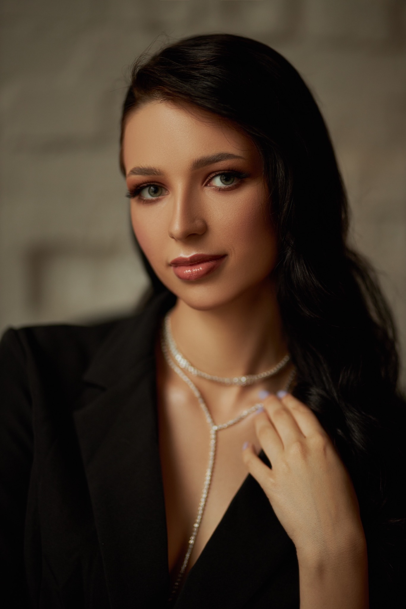 Portret kobiety z delikatnym makijażem i czarnymi włosami, wykonany w studiu w Łodzi, z widoczną biżuterią na szyi i czarną marynarką.